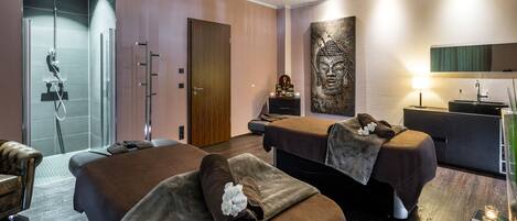 Une salle de spa équipée de deux tables de massage, d’un espace douche et d’une grande statue de Bouddha.