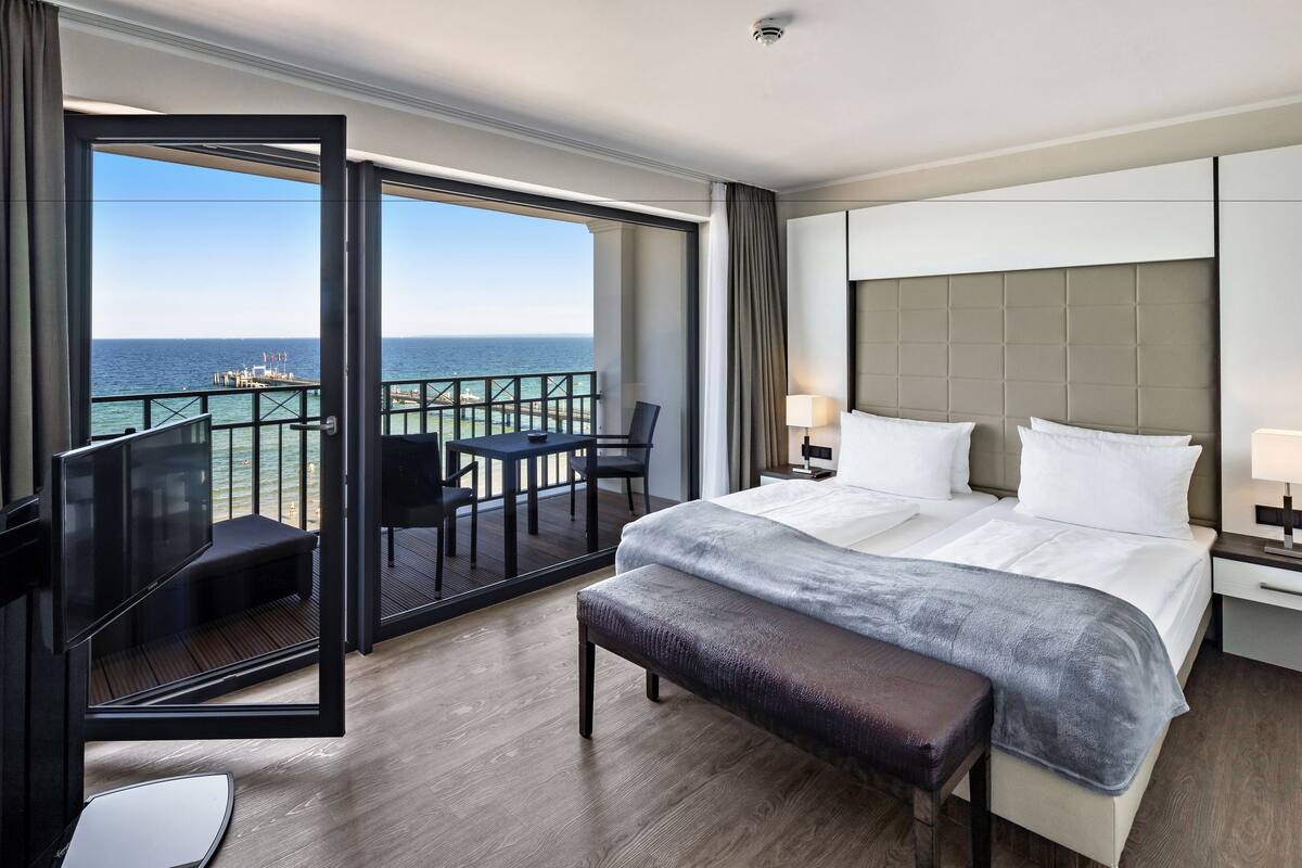 Une chambre d’hôtel avec un grand lit, une banquette, un bureau et un balcon donnant sur l’océan.