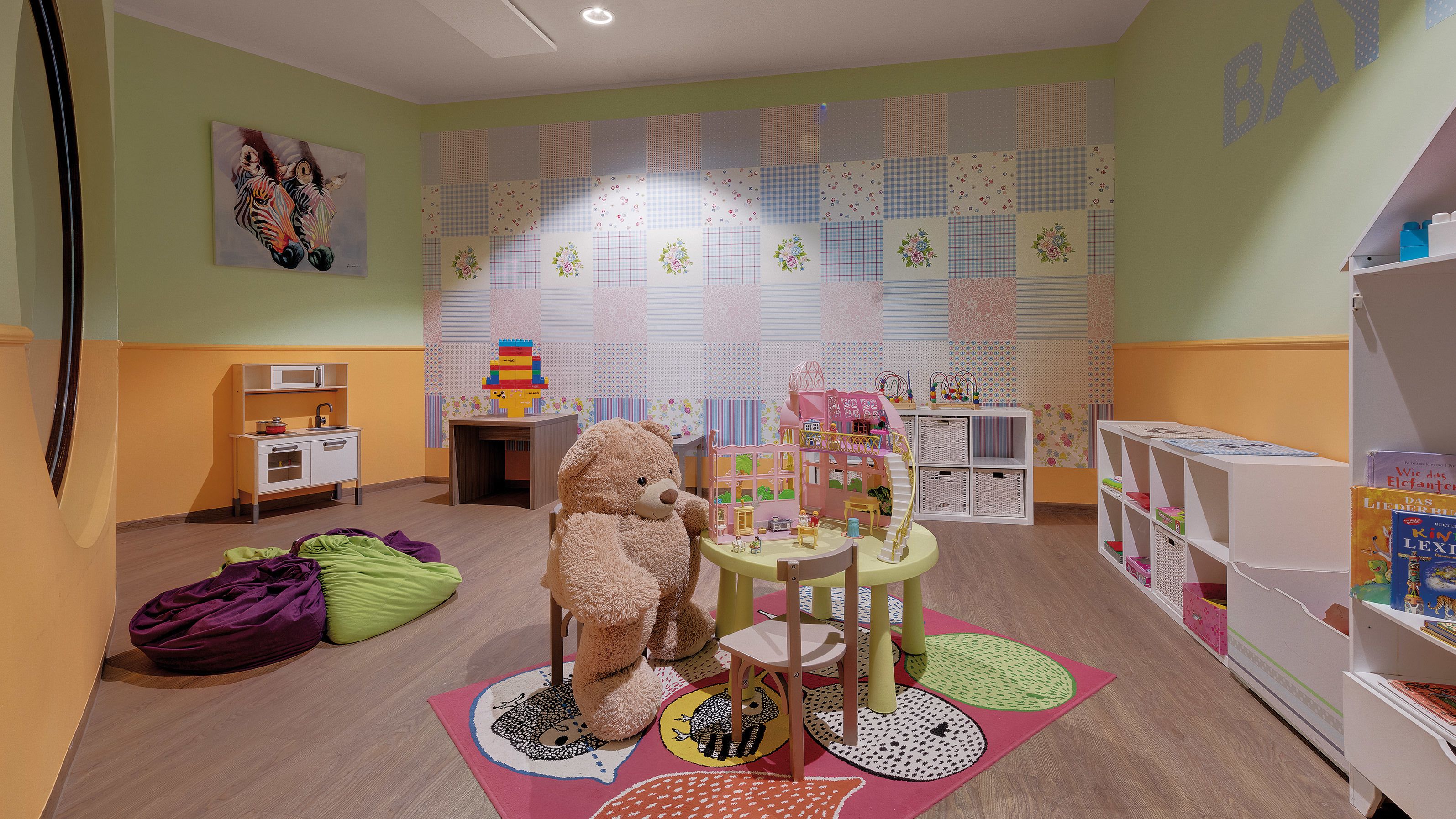A children's playroom with a large teddy bear, a play kitchen, and a bookshelf with books.