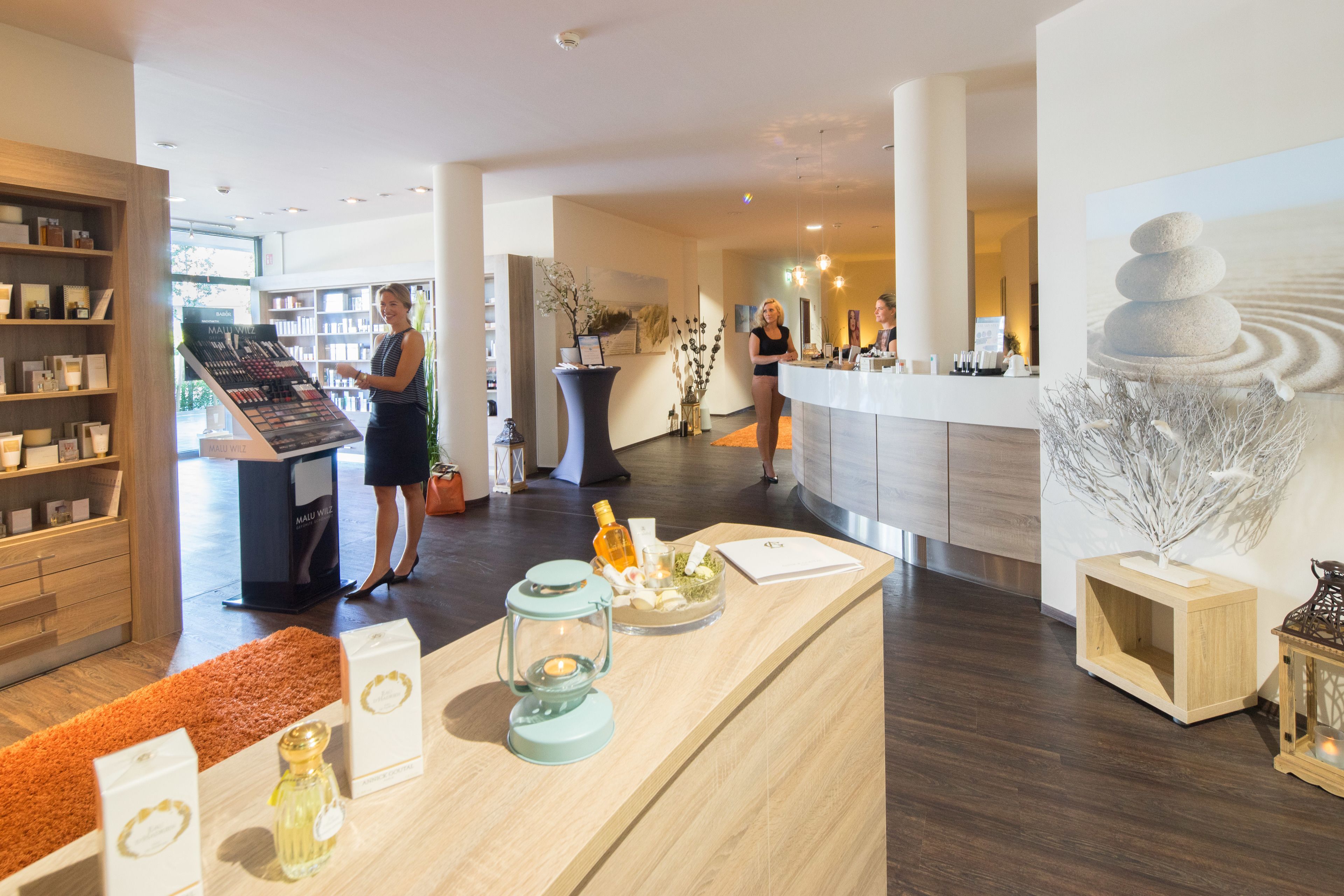 A modern hotel lobby with a reception desk, a display of toiletries, and a large decorative sculpture.
