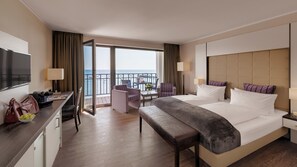 Quarto de hotel com uma cama grande, uma escrivaninha com computador, uma cadeira e uma varanda com vista para o mar.