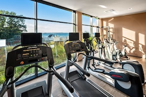 A gym with cardio equipment, large windows, and a view of the sea.