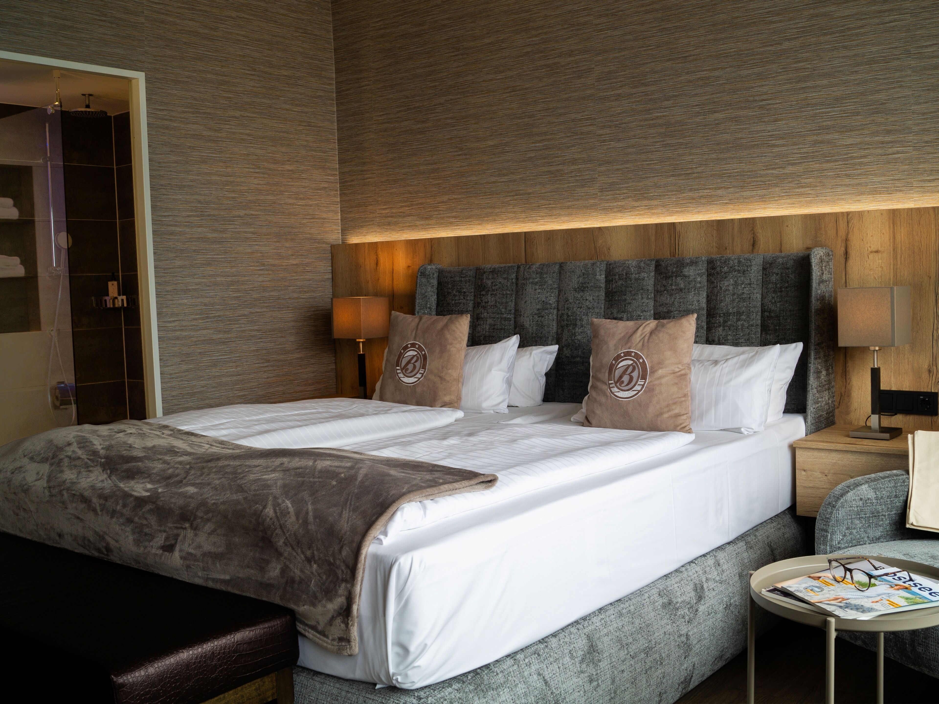 A hotel room with a large bed, two bedside tables, a small round table, and a bench.
