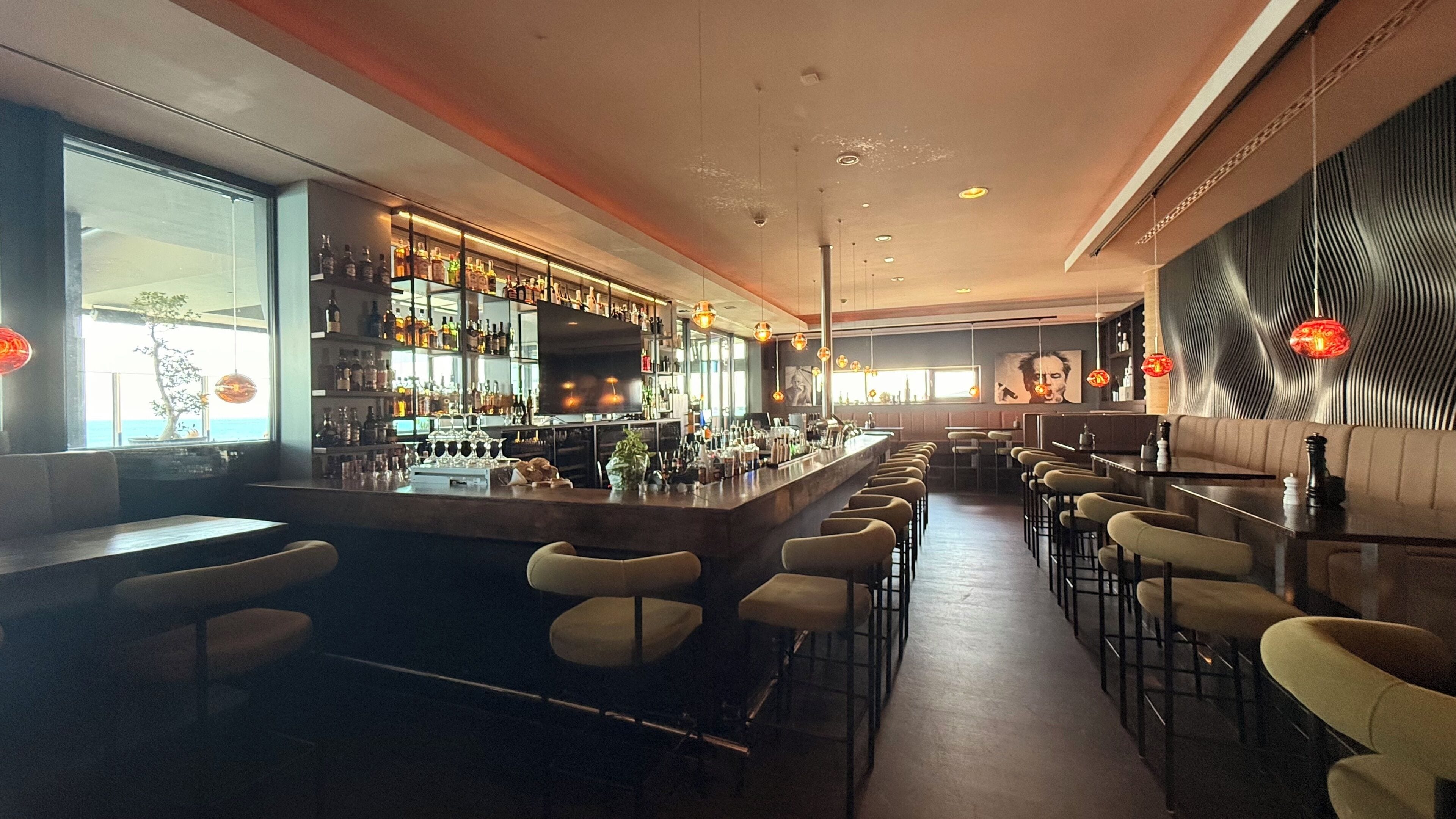 Eine Bar mit einer langen Theke, mehreren Hockern und einer Auswahl an Flaschen und Gläsern.