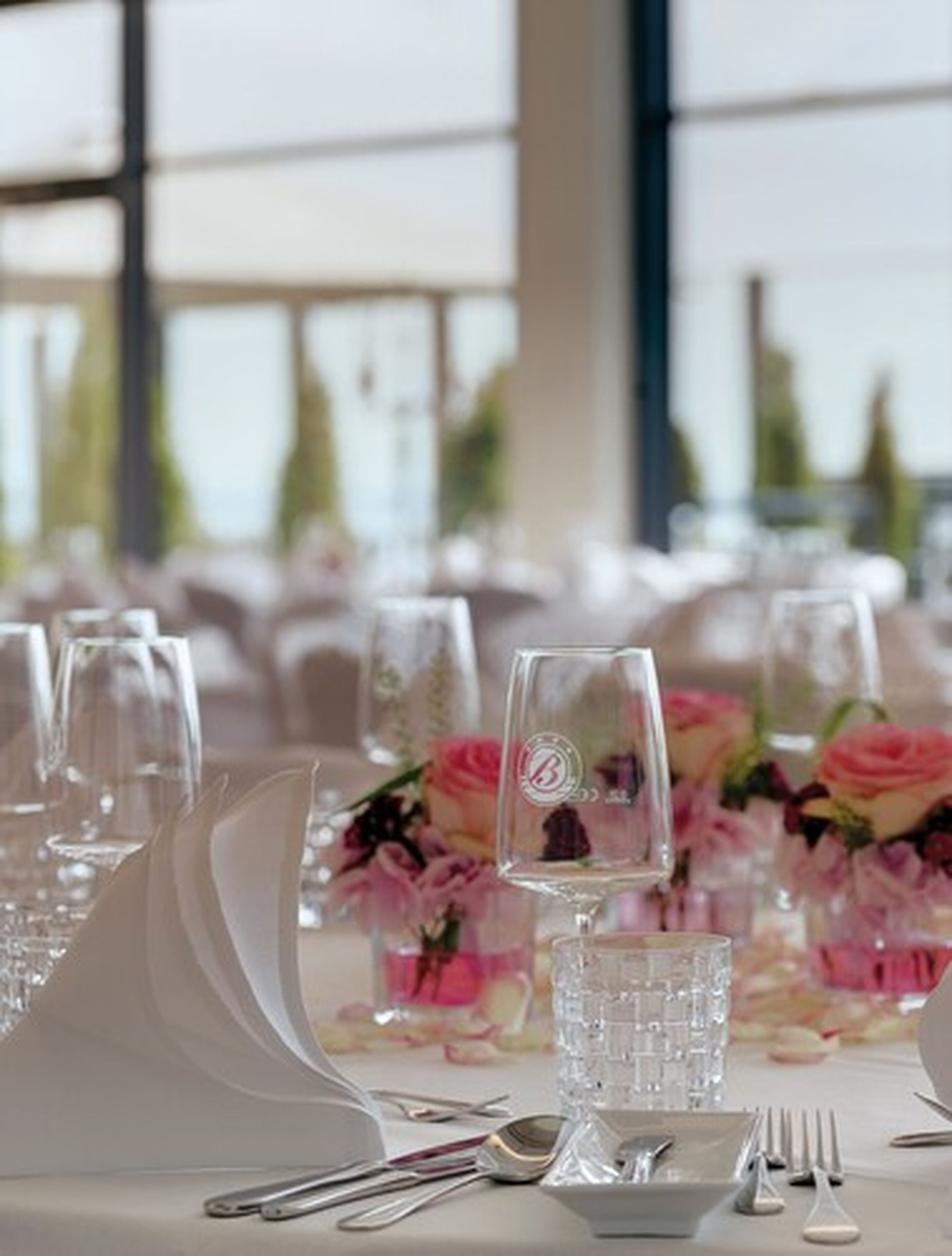 A table set for a formal event with clear glassware, silverware, and pink floral centerpieces.
