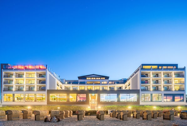 A multi-story hotel with a central atrium, large windows, and a sandy ground floor. - Bayside (Scharbeutz)