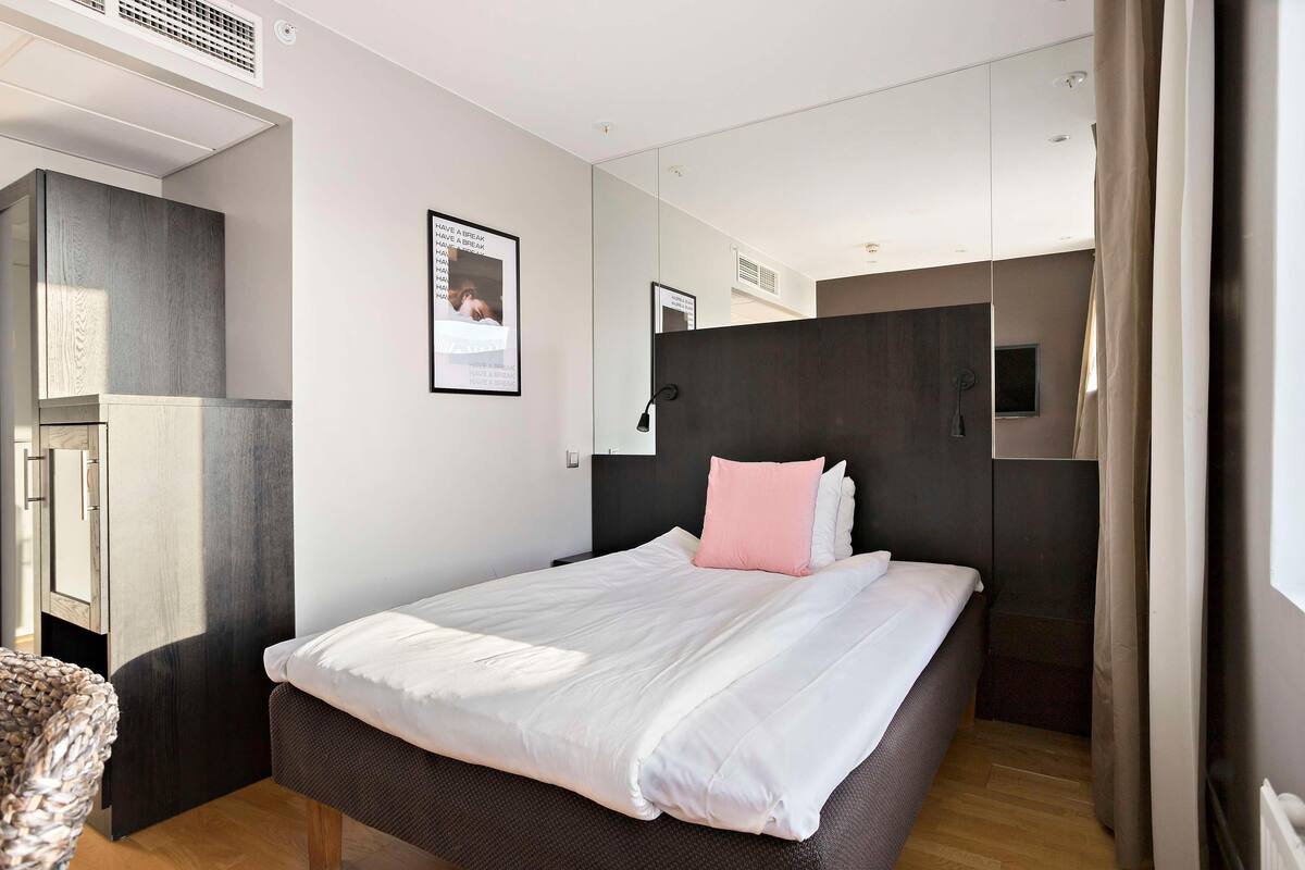 Ein modernes Hotelzimmer mit einem großen Bett, einem Kleiderschrank, einem Spiegel und einem kleinen Fenster.