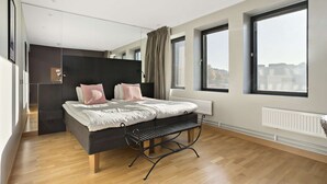 Ein modernes Schlafzimmer mit Bett, Sitzbank, großen Fenstern und Blick auf die Stadt.