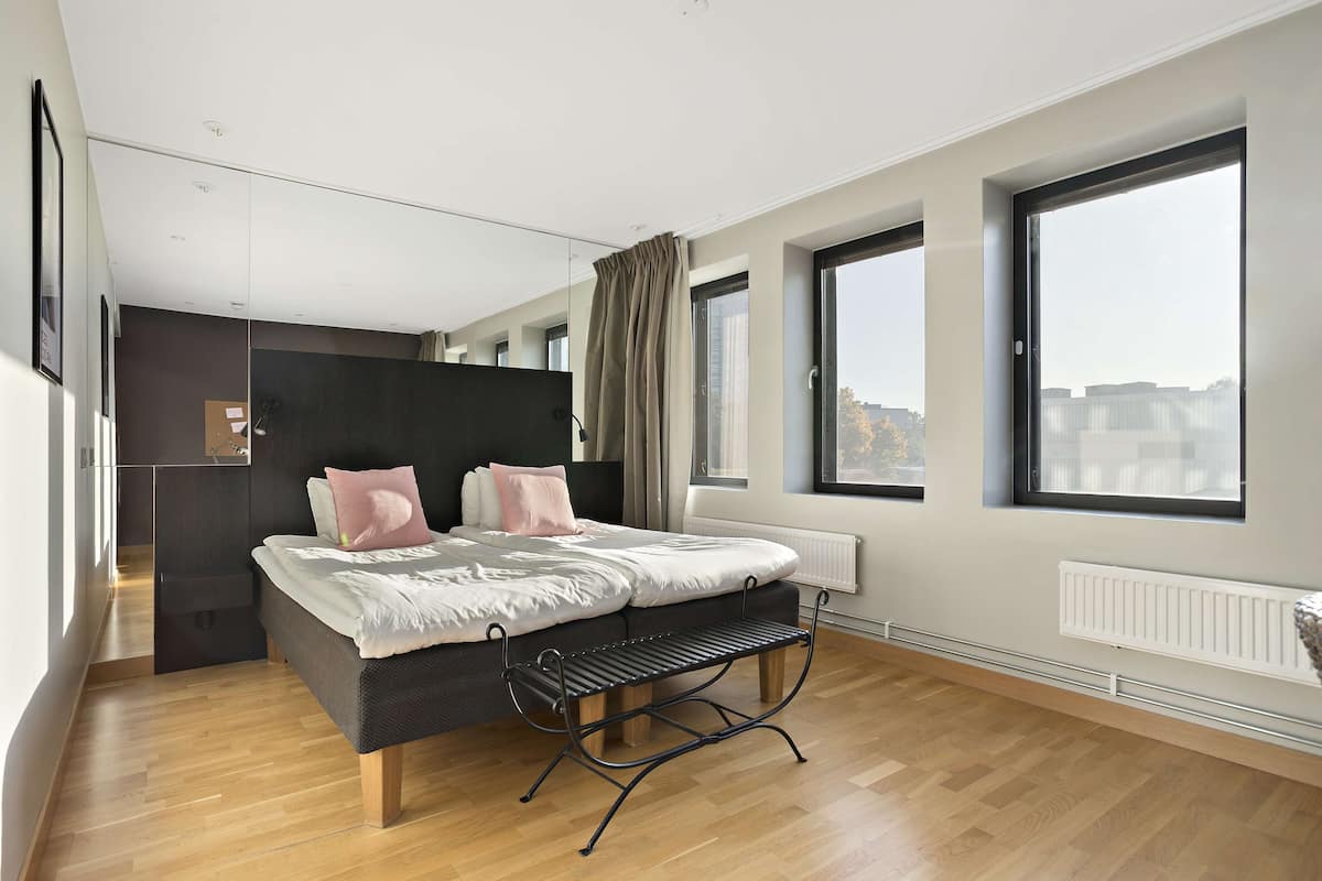 Ein modernes Schlafzimmer mit Bett, Sitzbank, großen Fenstern und Blick auf die Stadt.