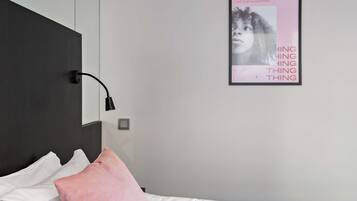 A bedroom with a bed, a bedside lamp, a poster on the wall, and a pillow.