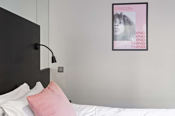 Un dormitorio con una cama, una lámpara de noche, un cartel en la pared y un almohadón.