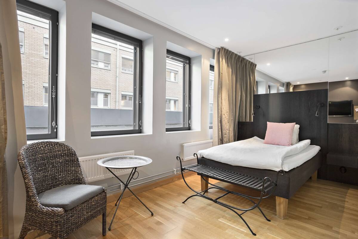 Ein modernes Schlafzimmer mit einem Bett, einem Sessel, einem kleinen Tisch und großen Fenstern.