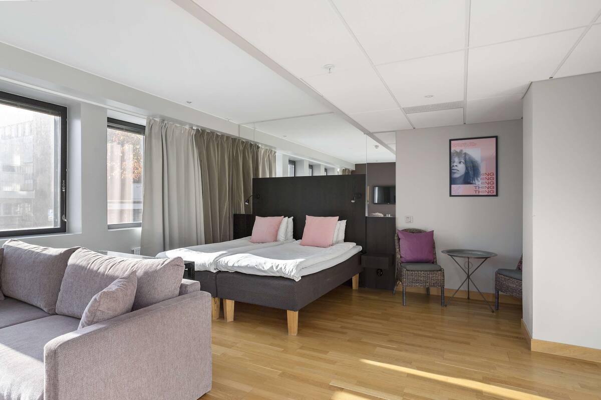 Ein modernes Hotelzimmer mit einem großen Bett, einer Couch, einem kleinen Tisch und Blick auf die Stadt.