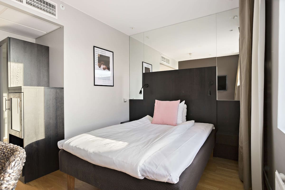 Ein modernes Hotelzimmer mit einem großen Bett, einem Kleiderschrank, einem Spiegel und einem kleinen Fenster.