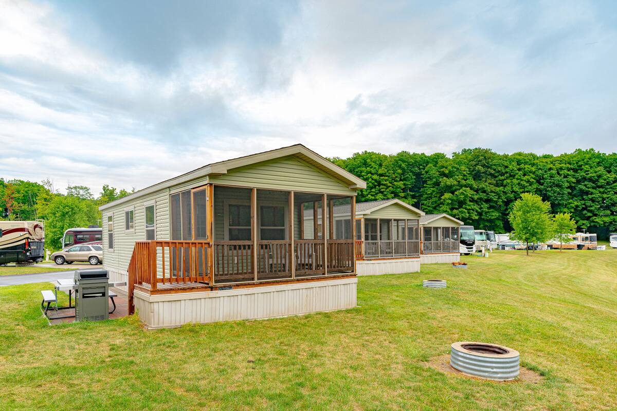 A mobile home with a porch and screened windows, surrounded by a grassy area and other mobile homes.