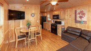 A wooden interior with a dining table, chairs, a sofa, a kitchen with appliances, and a ceiling fan. - Sun Retreats Gun Lake (Hopkins)