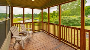 A wooden deck with two Adirondack chairs, a view of a lake, and a grassy area with trees. - Sun Retreats Gun Lake (Hopkins)