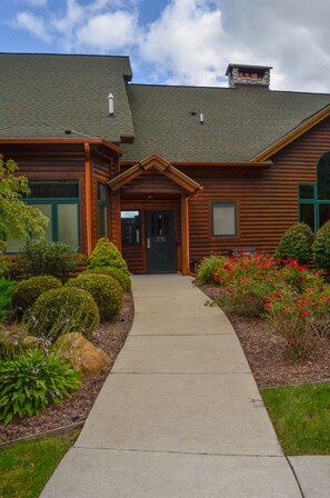 A log cabin with a covered porch, a chimney, and a well-maintained garden with various plants and flowers. - Sun Retreats Gun Lake (Hopkins)