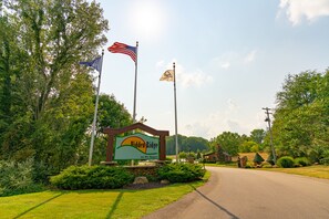 A sign for Hidden Ridge RV Resort with a road leading to it, surrounded by greenery and trees. - Sun Retreats Gun Lake (Hopkins)