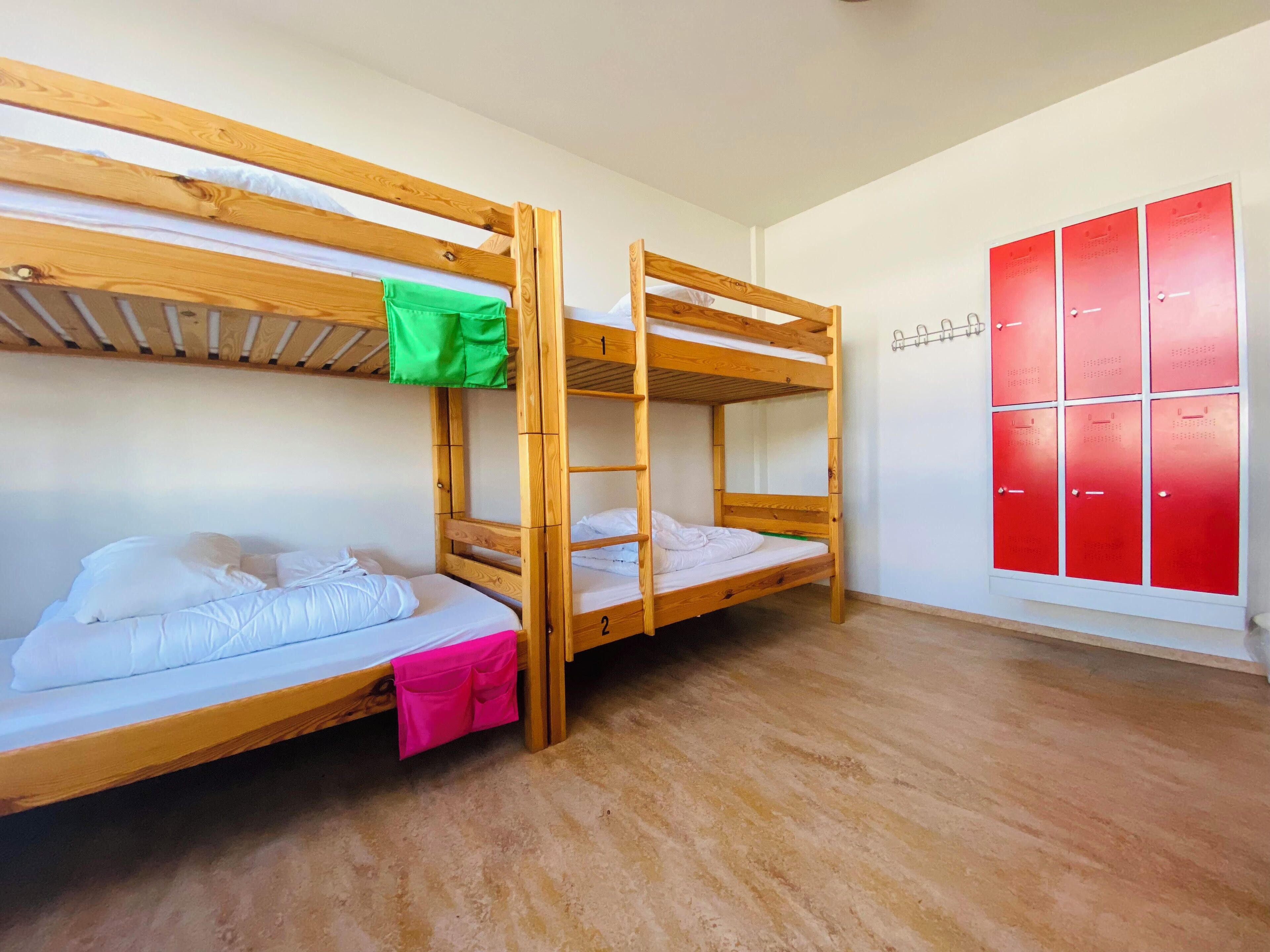 A bunk bed room with a wooden floor, white walls, and a red storage unit.