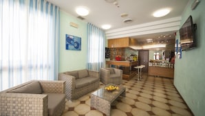 A modern living room with a sofa, armchairs, and a coffee table. There is a kitchen area with a bar and a television. - Hotel Luciana (Rimini)