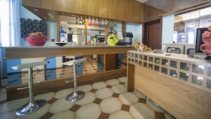 A modern kitchen with wooden cabinets, a bar area with stools, and a tiled floor. - Hotel Luciana (Rimini)