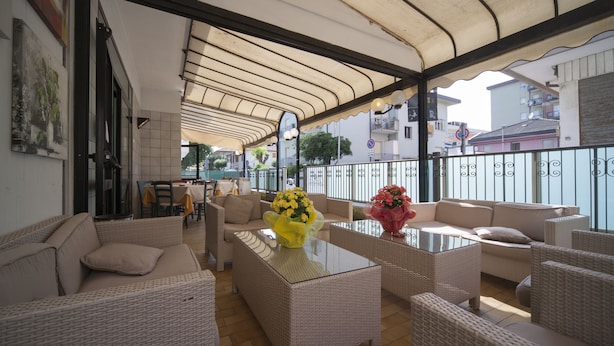 An outdoor seating area with wicker furniture and a glass table, featuring a view of the cityscape. - Hotel Luciana (Rimini)
