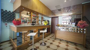 Zona bar moderna con bancone in legno, sgabelli e pavimento piastrellato.