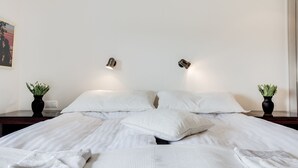A neatly made bed with white linens and pillows, two bedside tables with potted plants, and wall-mounted lights. - Guesthouse Bjarney (Selfoss)