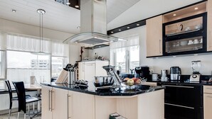 A modern kitchen with a central island, black appliances, and a dining area with a table and chairs. - Guesthouse Bjarney (Selfoss)