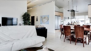 A modern living room with a white sofa, a dining area with wooden chairs, a large flat-screen TV, and a potted plant. - Guesthouse Bjarney (Selfoss)
