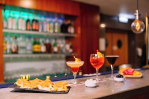 A bar area with a counter displaying food and drinks, a shelf with bottles, and a hanging light fixture. - Grand Muthu Forte do Vale (Albufeira)