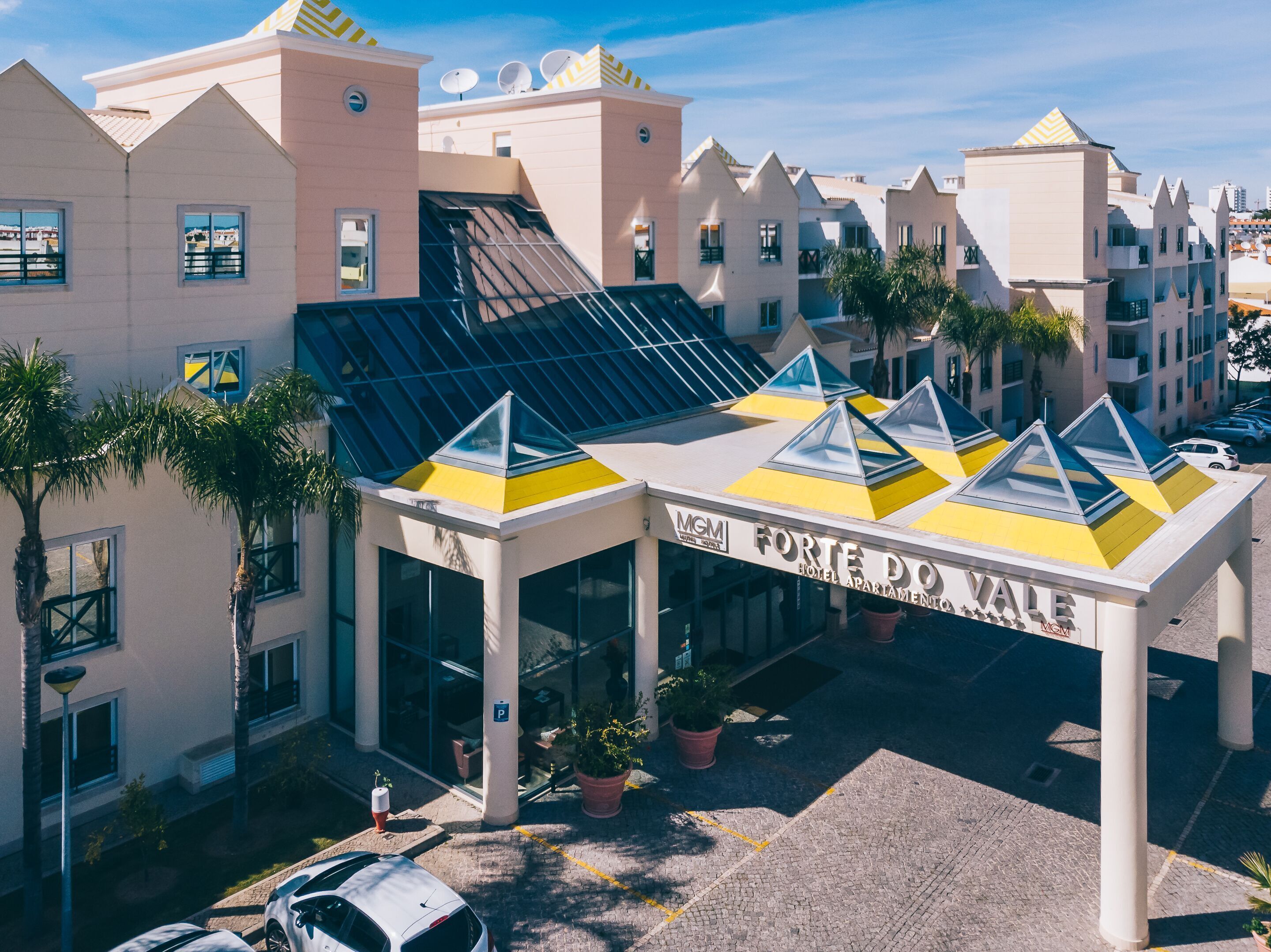 A hotel with a modern design, featuring a prominent entrance with a glass facade and a yellow and blue roof.