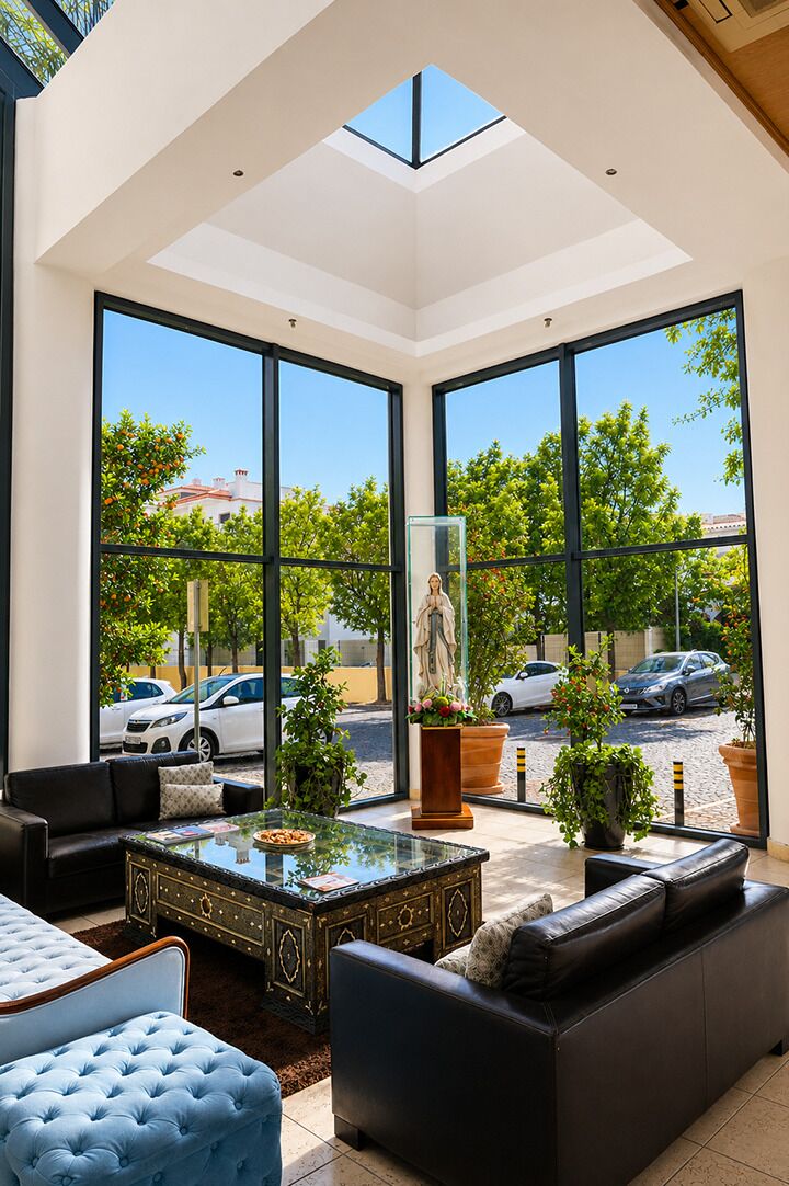 A spacious living area with a high ceiling, large windows, a glass coffee table, and a statue.