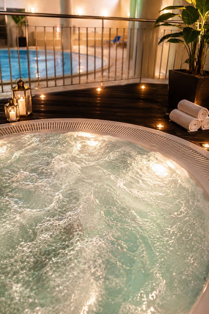 A hot tub with a railing, a potted plant, and a pool in the background.