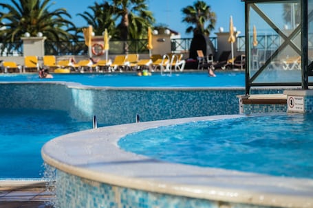 Una piscina techada, una piscina al aire libre, sombrillas