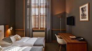 A hotel room with a bed, a desk, a chair, a TV, and a window with blinds. - YoHo - the young hotel (Hamburg)