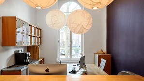 A modern office with a wooden desk, an Apple laptop, and a desktop computer. There are paper lanterns hanging from the ceiling and a window with a view of the street. - YoHo - the young hotel (Hamburg)