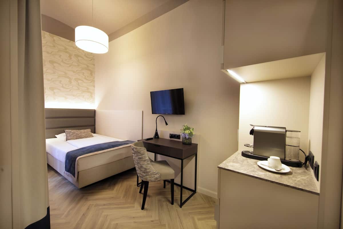 Una habitación de hotel moderna con cama, escritorio, silla, televisor y cafetera.