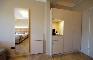 Quarto de hotel com cama, guarda-roupa e espelho refletindo o ambiente.