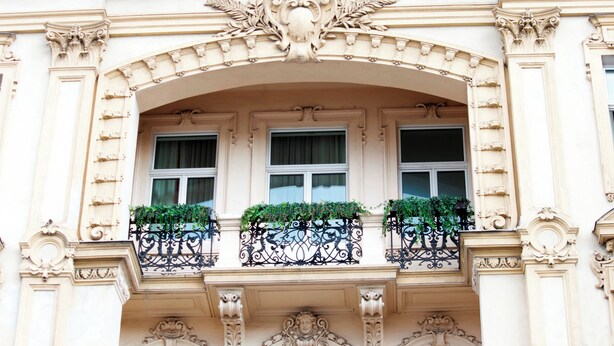 Une façade d’immeuble ornée de détails architecturaux raffinés, notamment une arche décorative au-dessus des fenêtres et un balcon doté de balustrades en fer forgé.