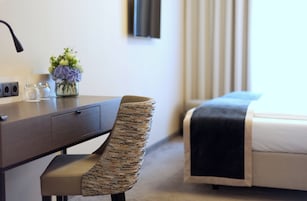 Una camera d'albergo con un letto, una scrivania con una sedia, un vaso con fiori e un televisore appeso al muro.