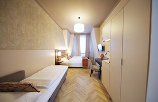 Quarto de hotel com duas camas, uma escrivaninha, uma cadeira, uma televisão e um guarda-roupa.