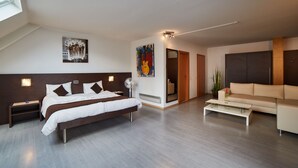 Una habitación de hotel moderna con una cama grande, un sofá, una mesa de centro y obras de arte en las paredes.