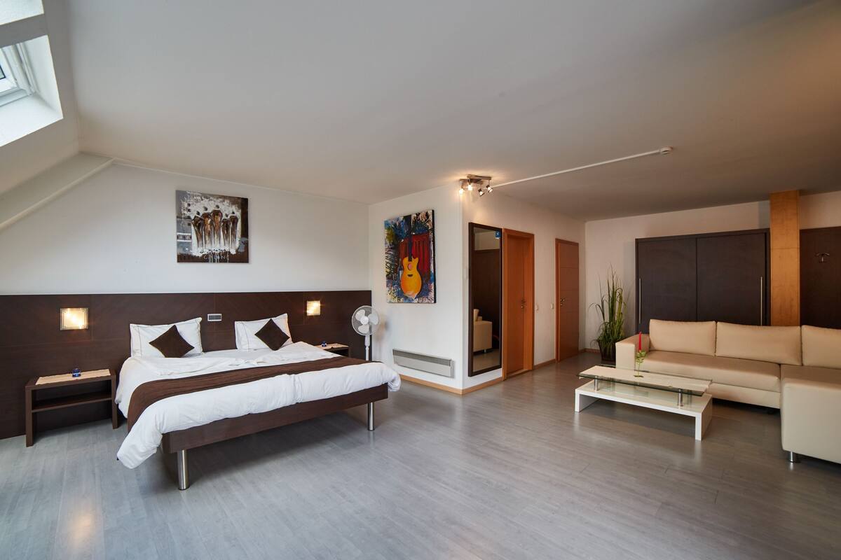 Moderni hotellihuone, jossa on suuri sänky, sohva, sohvapöytä ja taideteoksia seinillä.