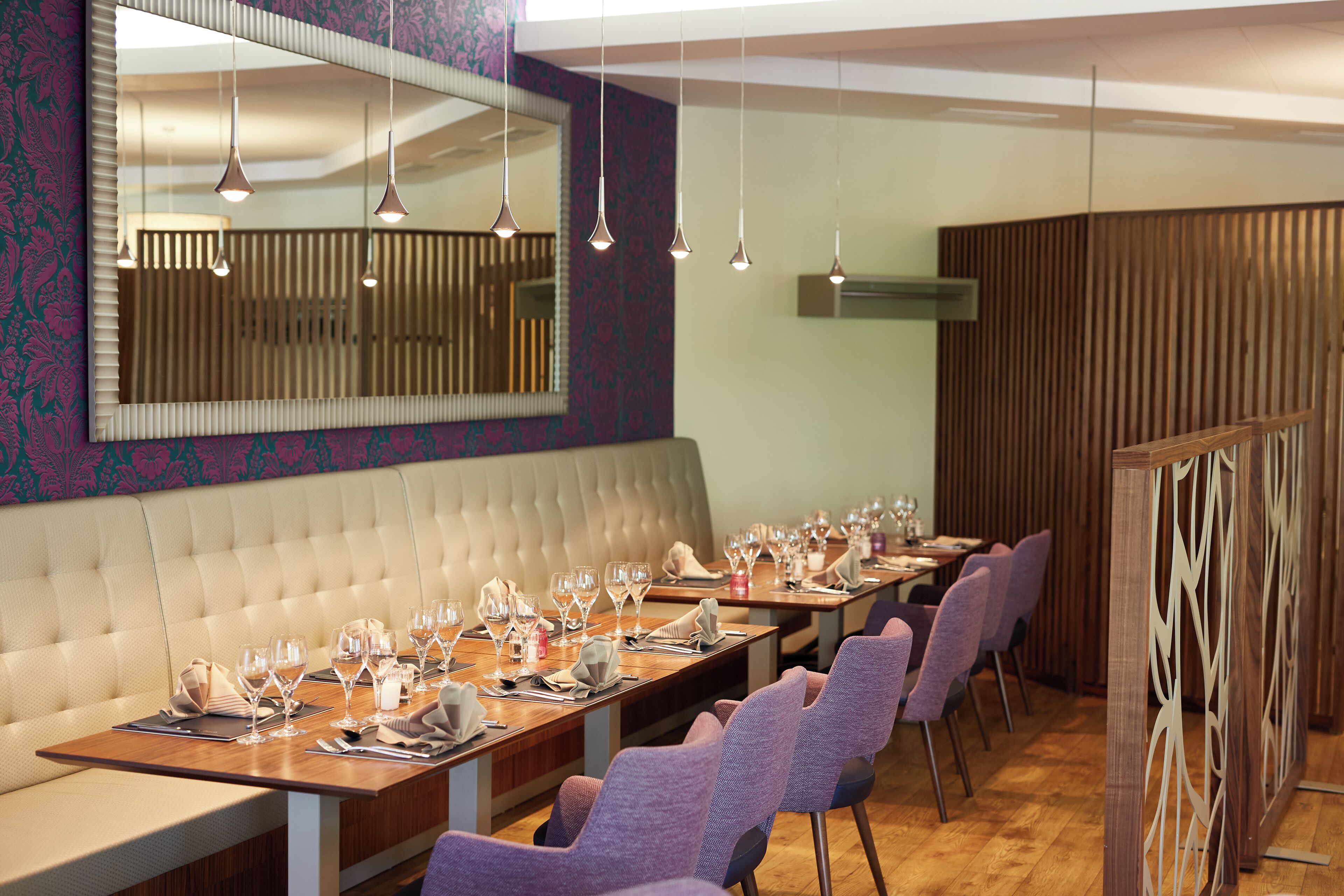 Ein Restaurant mit einem langen Holztisch, gedeckten Plätzen, einer gepolsterten Bank und violetten Stühlen.