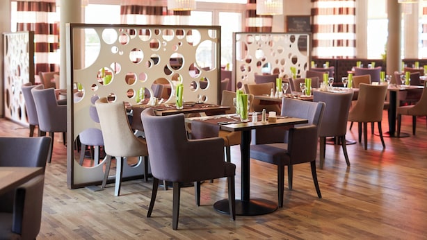 Un restaurante con mesas redondas, sillas y piso de madera.