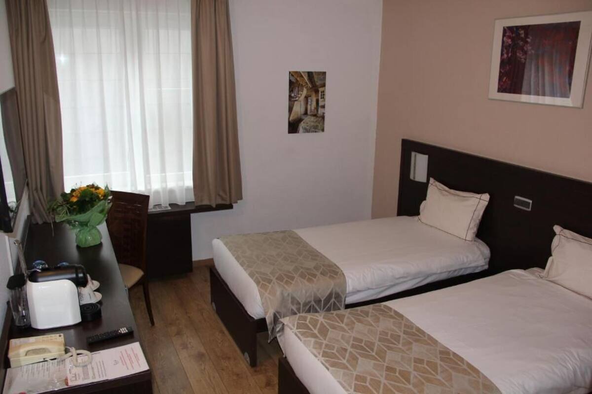 Hotellihuone, jossa on kaksi sänkyä, työpöytä, jossa on puhelin, maljakko kukkineen ja ikkuna, jossa on verhot.