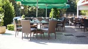 Un patio al aire libre con mesas y sillas, sombrillas verdes y plantas en macetas.