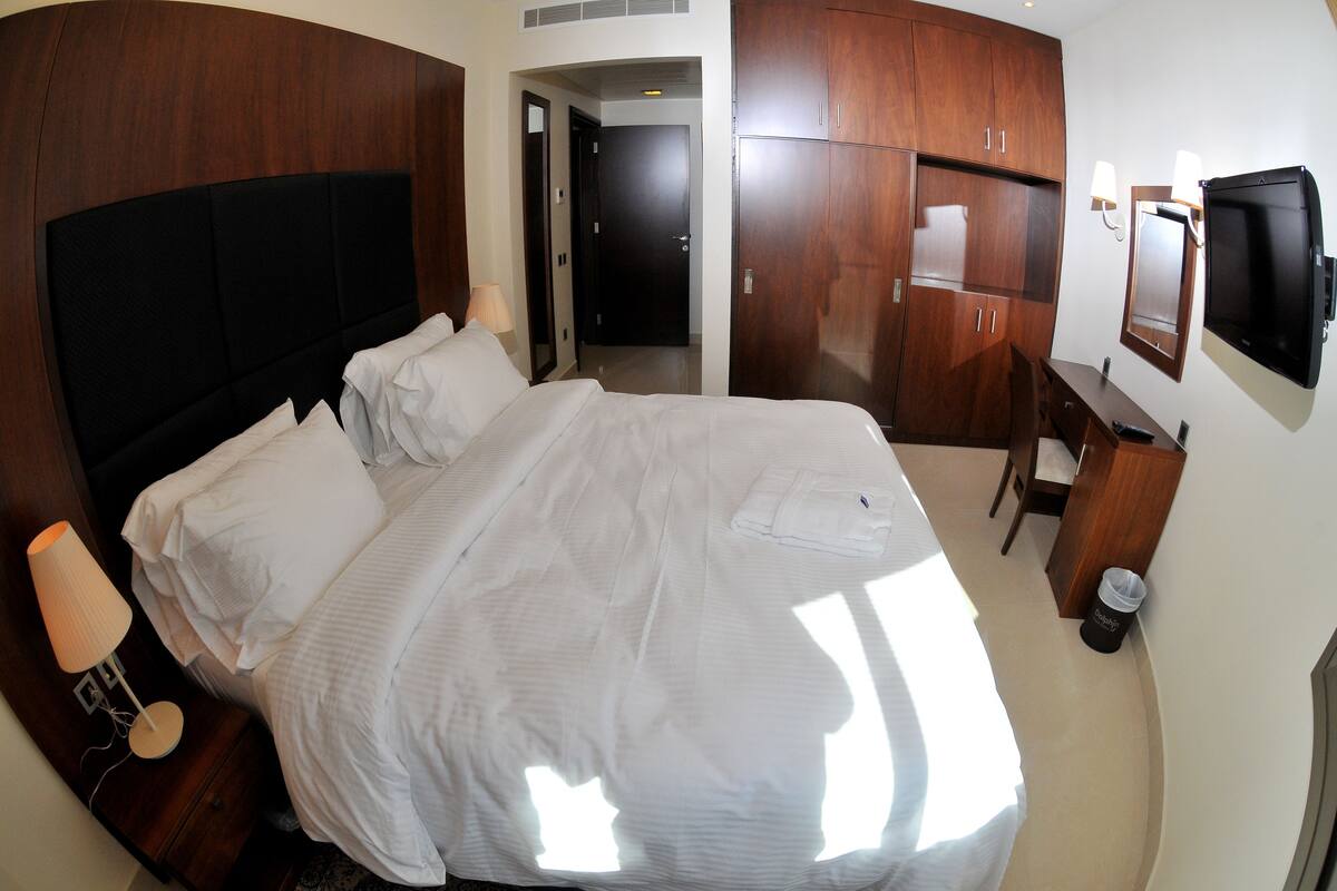 A hotel room with a large bed, a desk, a mirror, and a television.